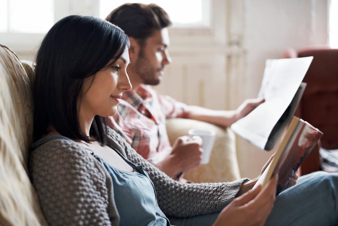 A couple sits together on a couch, both reading.