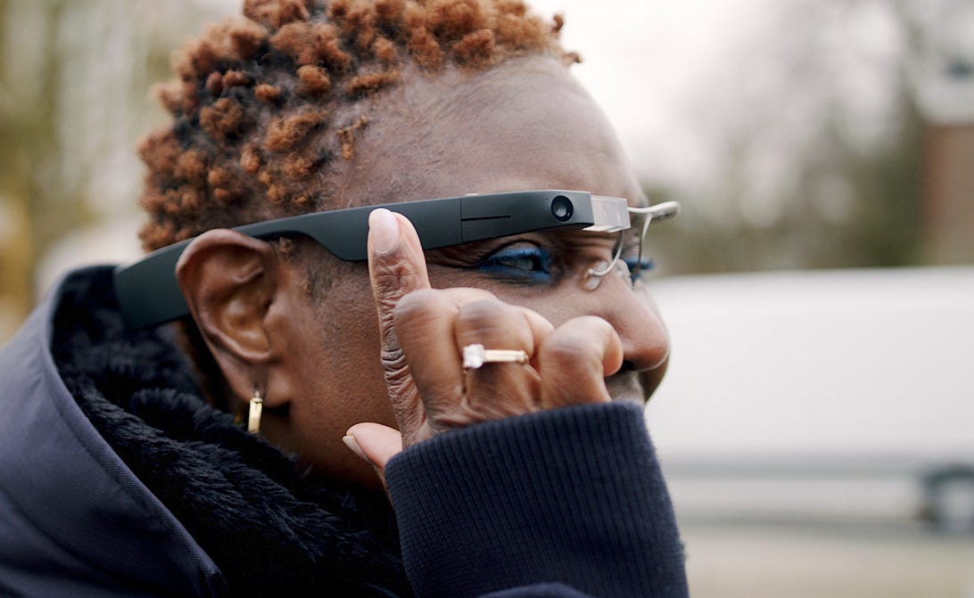 A woman wearing Envision glasses and reaching up to touch the frames.